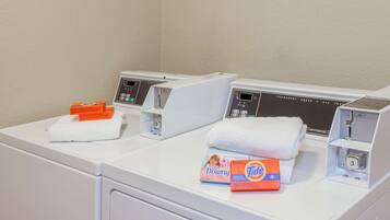 A laundry area with three washing machines, a white towel, and two detergent boxes.
