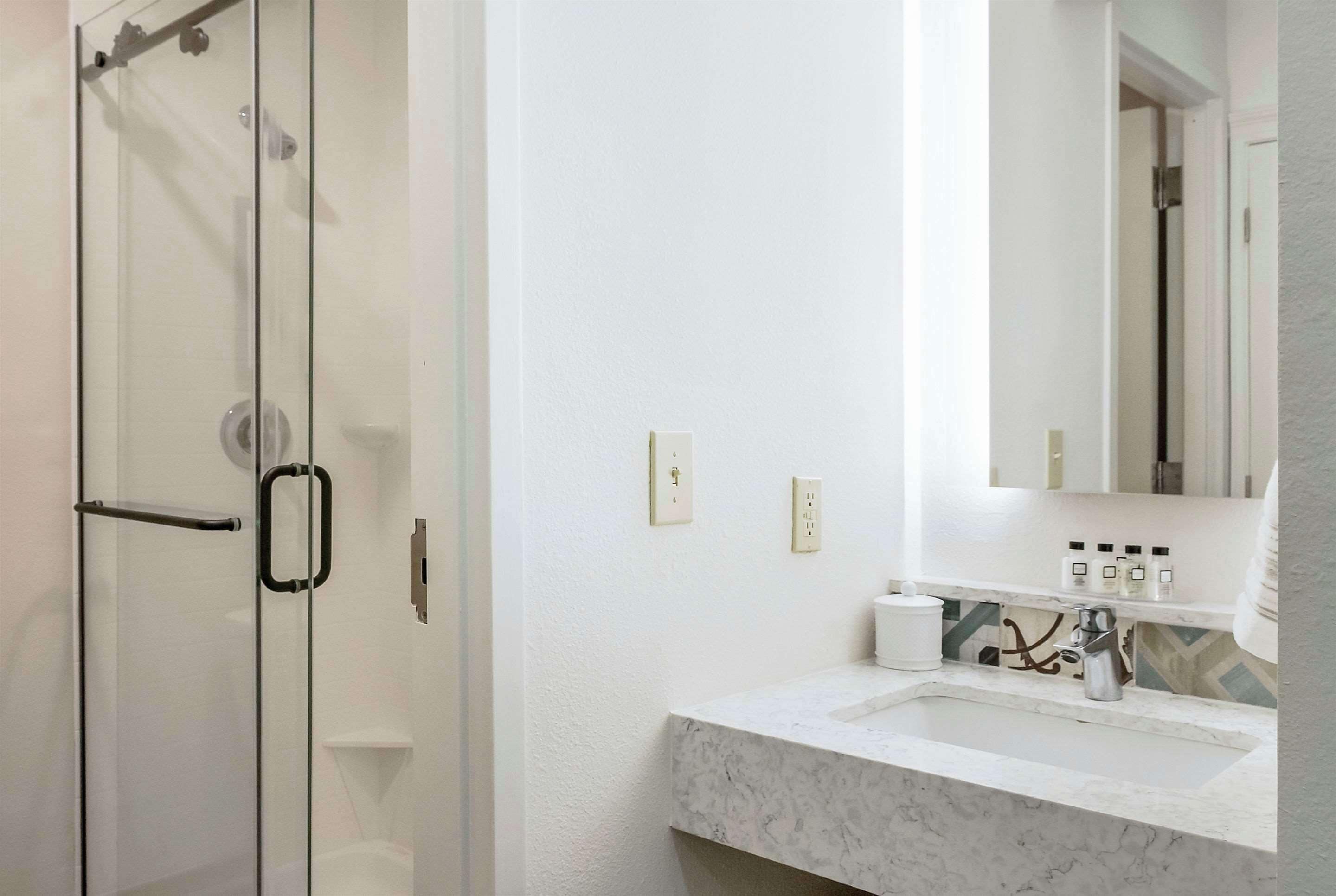 Une salle de bain moderne avec une douche à l’italienne en verre, un lavabo blanc doté d’un plan de toilette en marbre et un miroir au-dessus du lavabo.