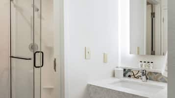 Une salle de bain dotée d’une douche à parois de verre, d’un lavabo blanc avec un plan de toilette en marbre et d’un miroir au-dessus du lavabo.