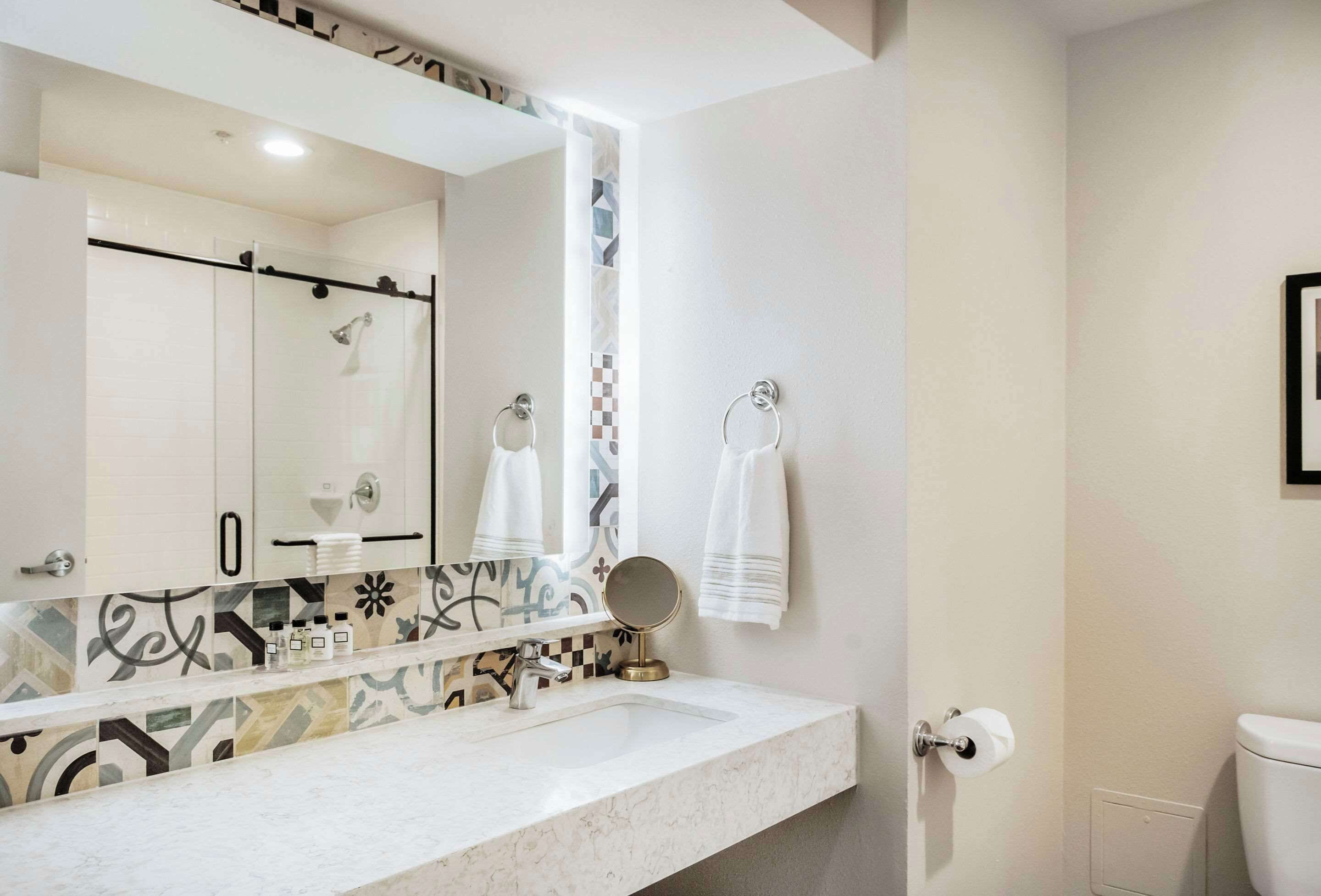 A bathroom with a white sink, a large mirror, a towel rack, and a toilet.