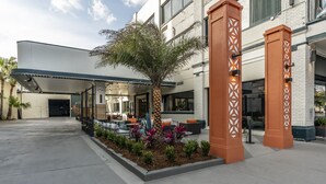 A hotel entrance with outdoor seating, palm trees, and decorative pillars. - St Charles Coach House, an Ascend Collection Hotel (New Orleans)