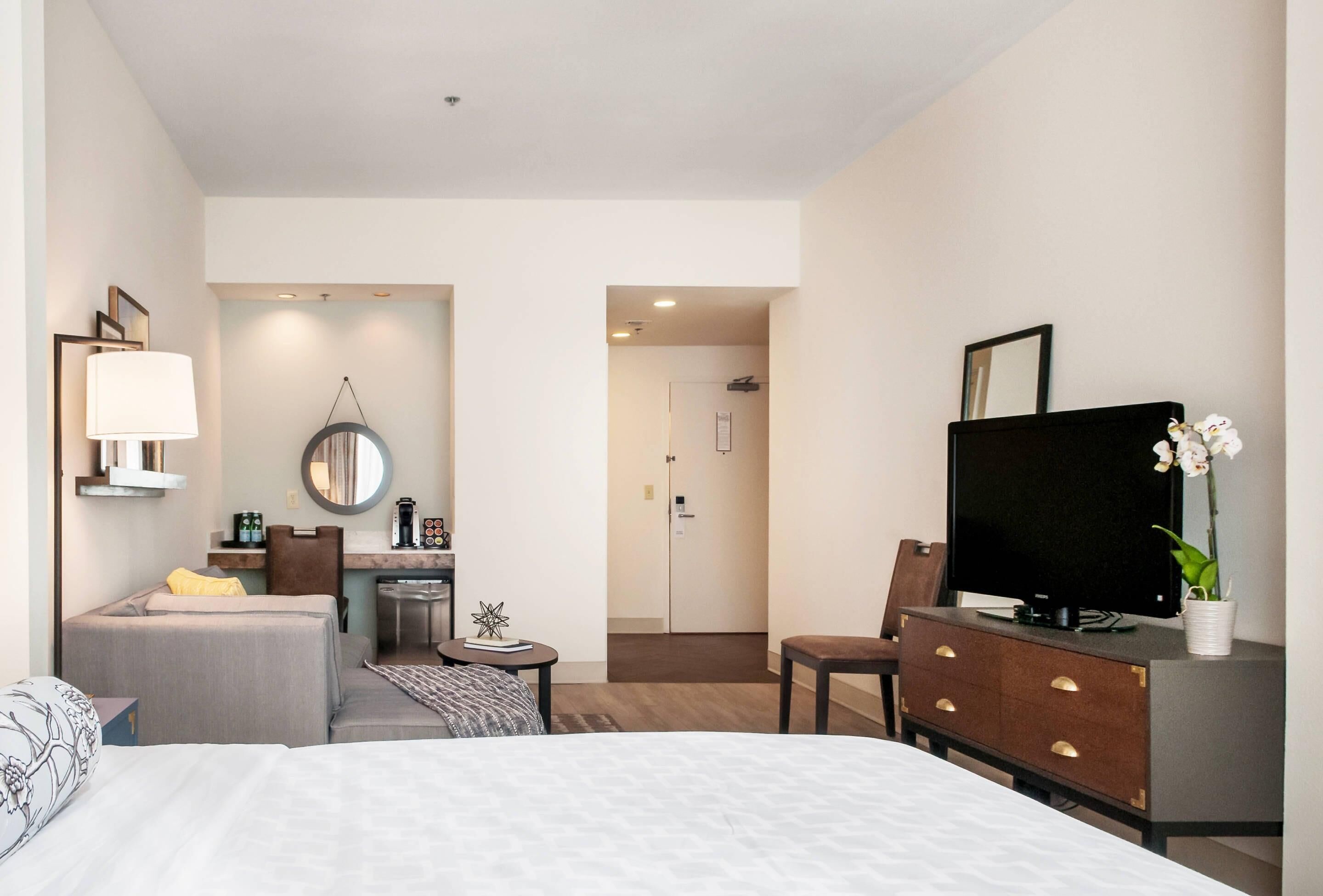 Ein Hotelzimmer mit einem Bett, einem Schreibtisch, einem Sessel, einem Fernseher und einem kleinen Tisch mit Lampe und Dekoration.