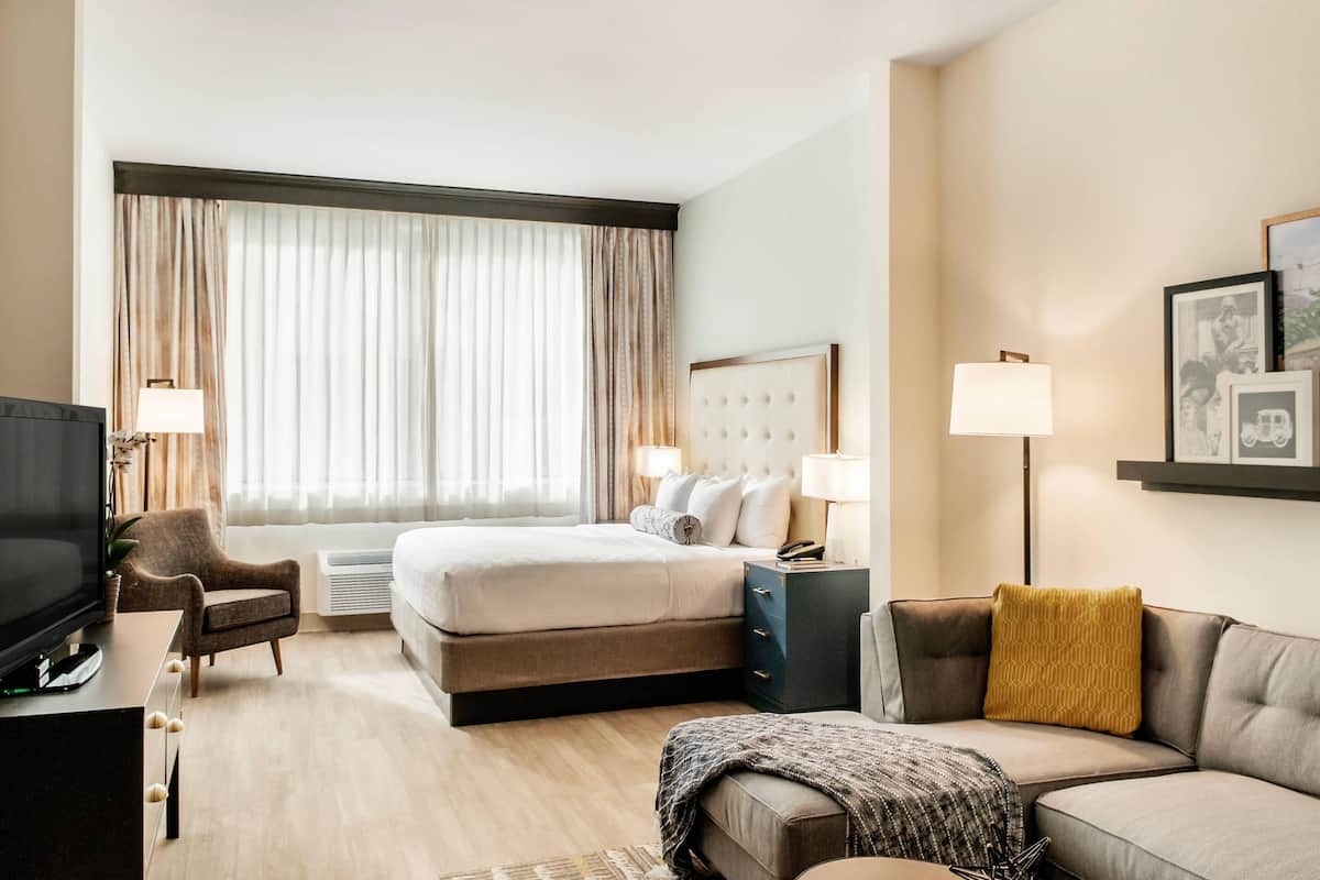 A hotel room with a bed, a sofa, a TV, a desk, and a window with curtains.