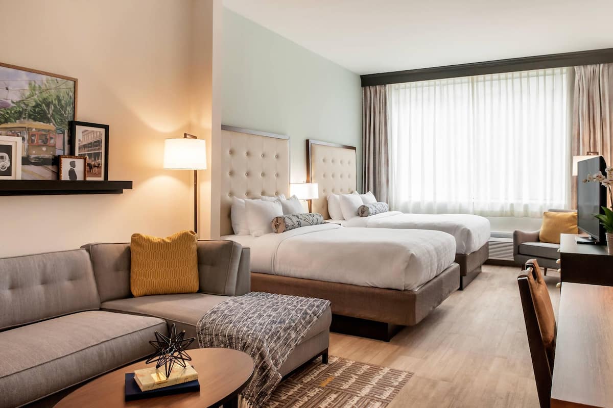 A hotel room with a sofa, two beds, a desk, and a TV.