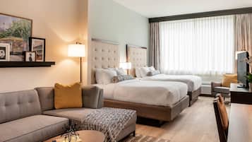 Ein Hotelzimmer mit einer Couch, zwei Betten, einem Schreibtisch und einem Fernseher.