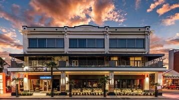 A hotel with a two-story facade, a balcony on the upper floor, and a ground-level entrance with a sign indicating it's now open.
