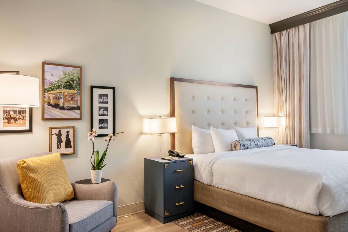 A hotel room with a bed, a chair, a nightstand, and wall art.