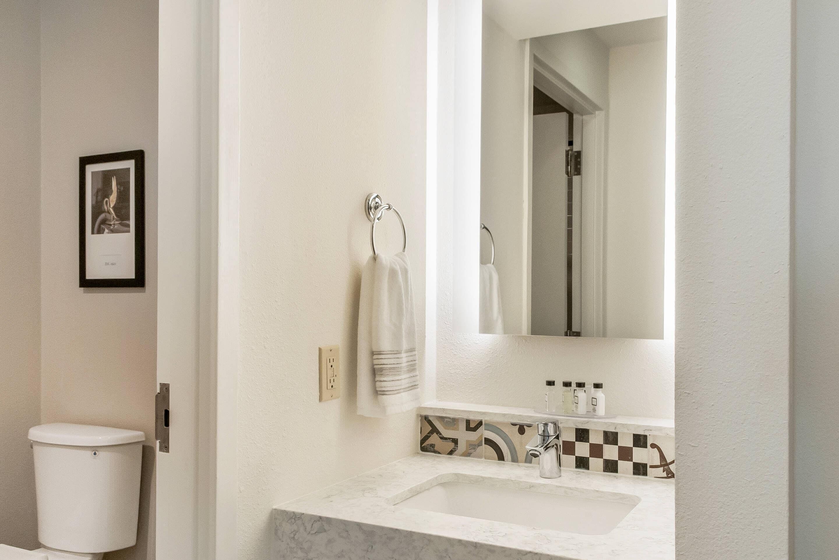 Een badkamer met een wit toilet, een wastafel met een spiegel erboven en een handdoek aan een ring.