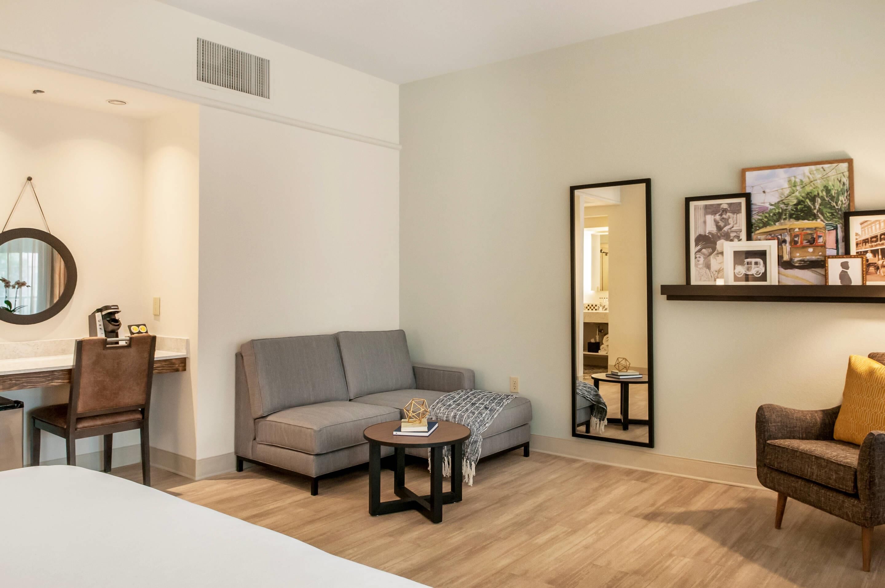A modern living room with a sofa, a coffee table, and a chair. There is a mirror on the wall and framed pictures above the sofa.