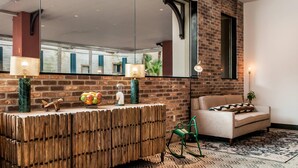 A modern living room with a brick wall, a large mirror, a wooden console table, a sofa, and a patterned rug. - St Charles Coach House, an Ascend Collection Hotel (New Orleans)