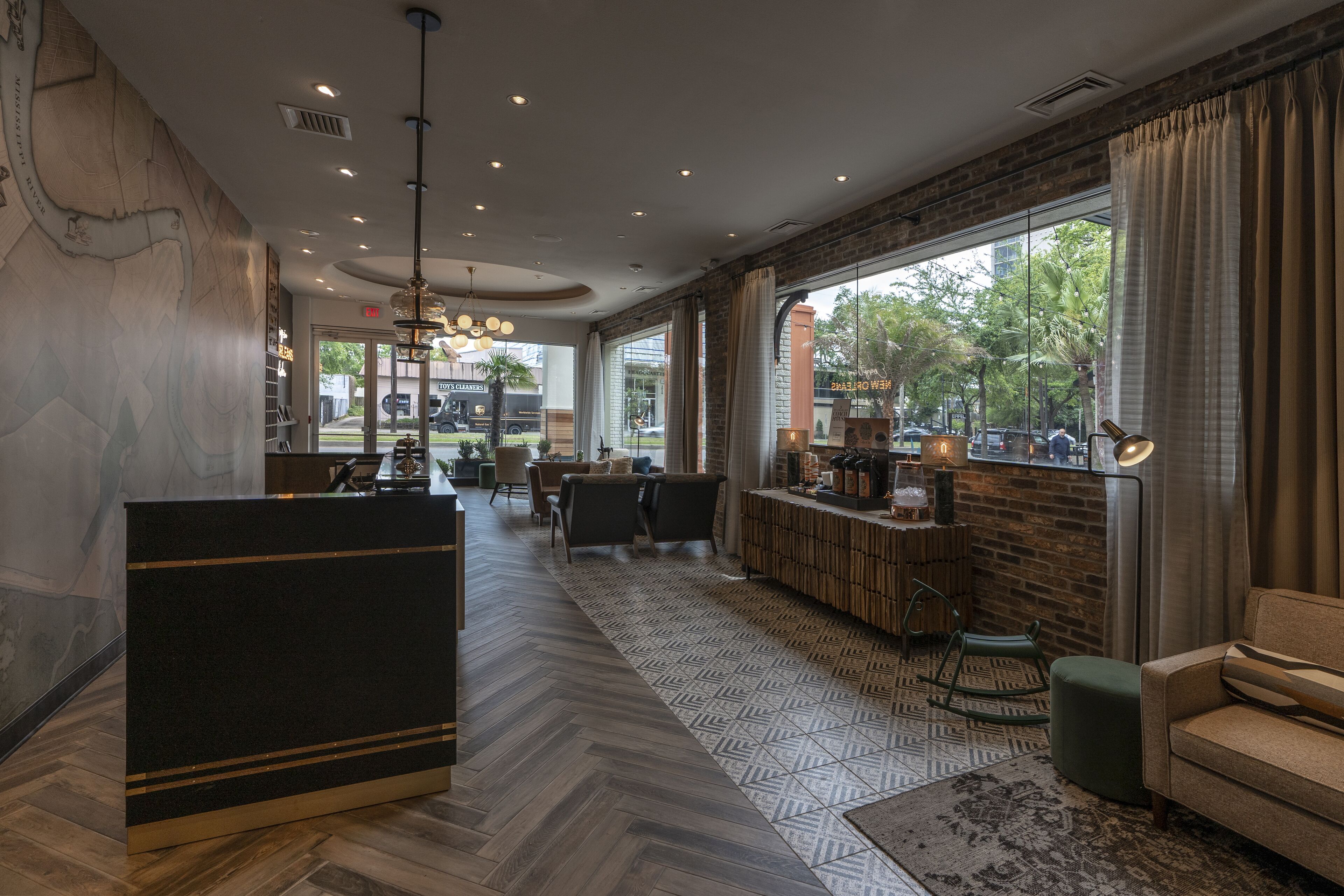 A modern hotel lobby with a reception desk, seating area, and large windows offering a view of the outdoors.