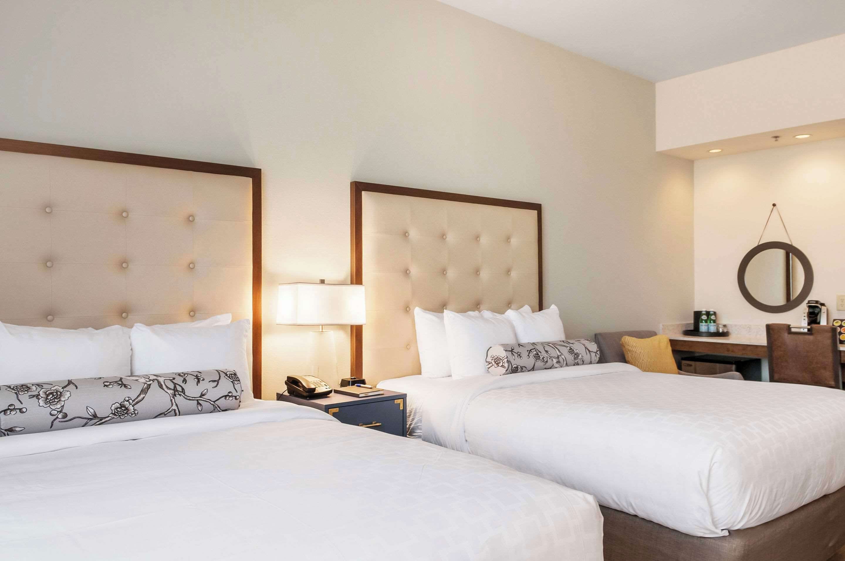 Une chambre d’hôtel avec deux lits, un bureau, une chaise, une lampe et un miroir rond accroché au mur.