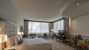A hotel room with a large bed, a desk, a chair, a TV, and a window with curtains. - St Charles Coach House, an Ascend Collection Hotel (New Orleans)