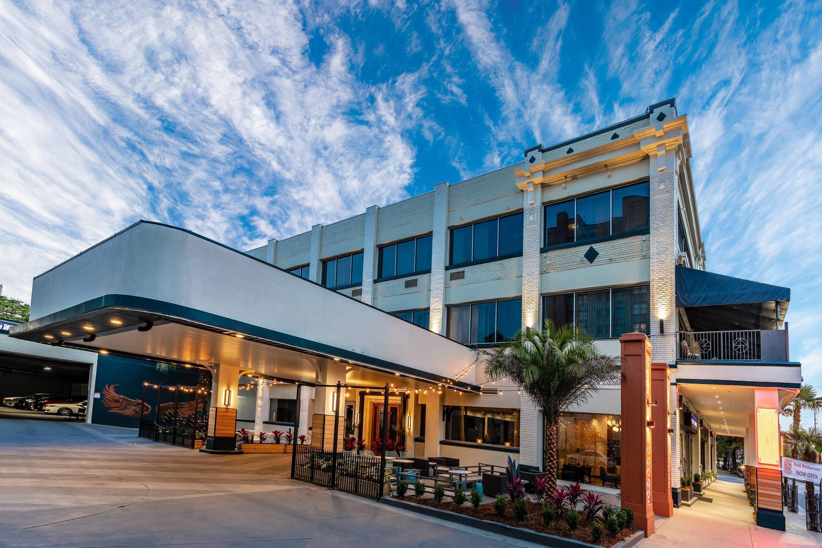 A hotel with a covered outdoor seating area, a parking garage, and a restaurant sign.