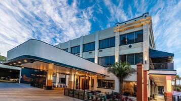 A hotel with a covered outdoor seating area, a parking garage, and a restaurant sign.