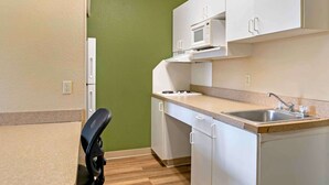 A compact kitchen with white cabinets, a microwave, a sink, and a chair. - Extended Stay America Suites Detroit Madison Heights (Madison Heights)