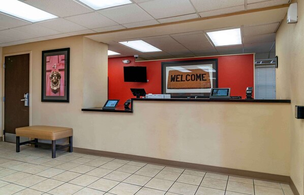 A reception area with a red wall, a welcome sign, a desk with a computer, and a bench.