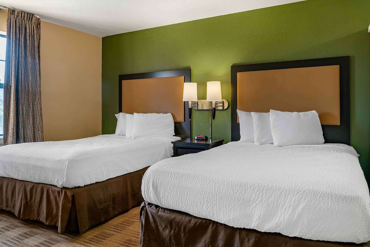 Ein Hotelzimmer mit zwei Betten, einem Nachttisch mit Lampen und einer grünen Wand.