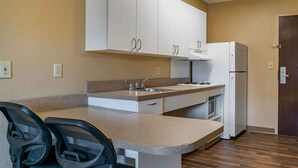 A compact kitchen with white cabinets, a sink, a refrigerator, and a microwave. There are two chairs at the counter.
