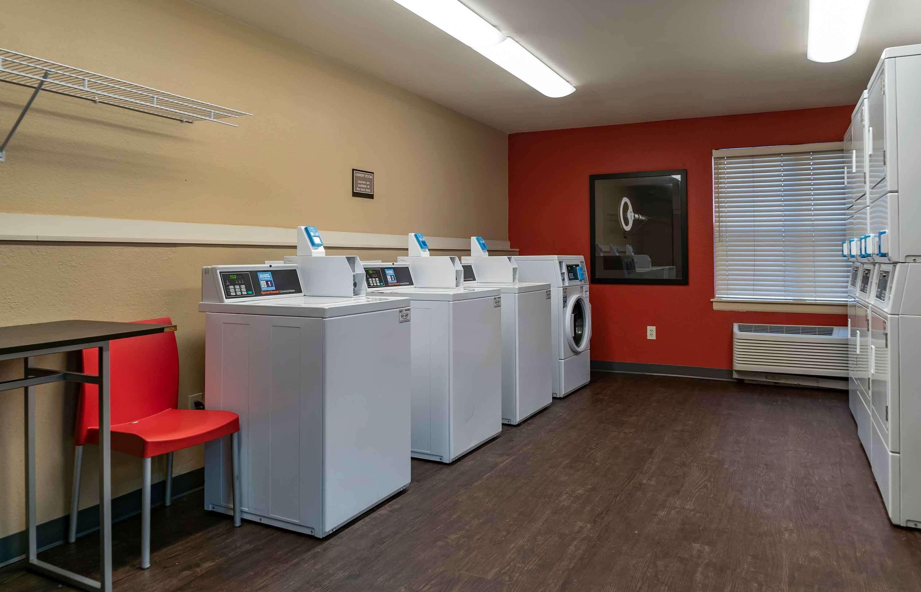A laundry room with four washing machines, a red chair, a table, and a wall-mounted drying rack.