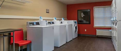 A laundry room with four washing machines, a red chair, a table, and a wall-mounted drying rack.