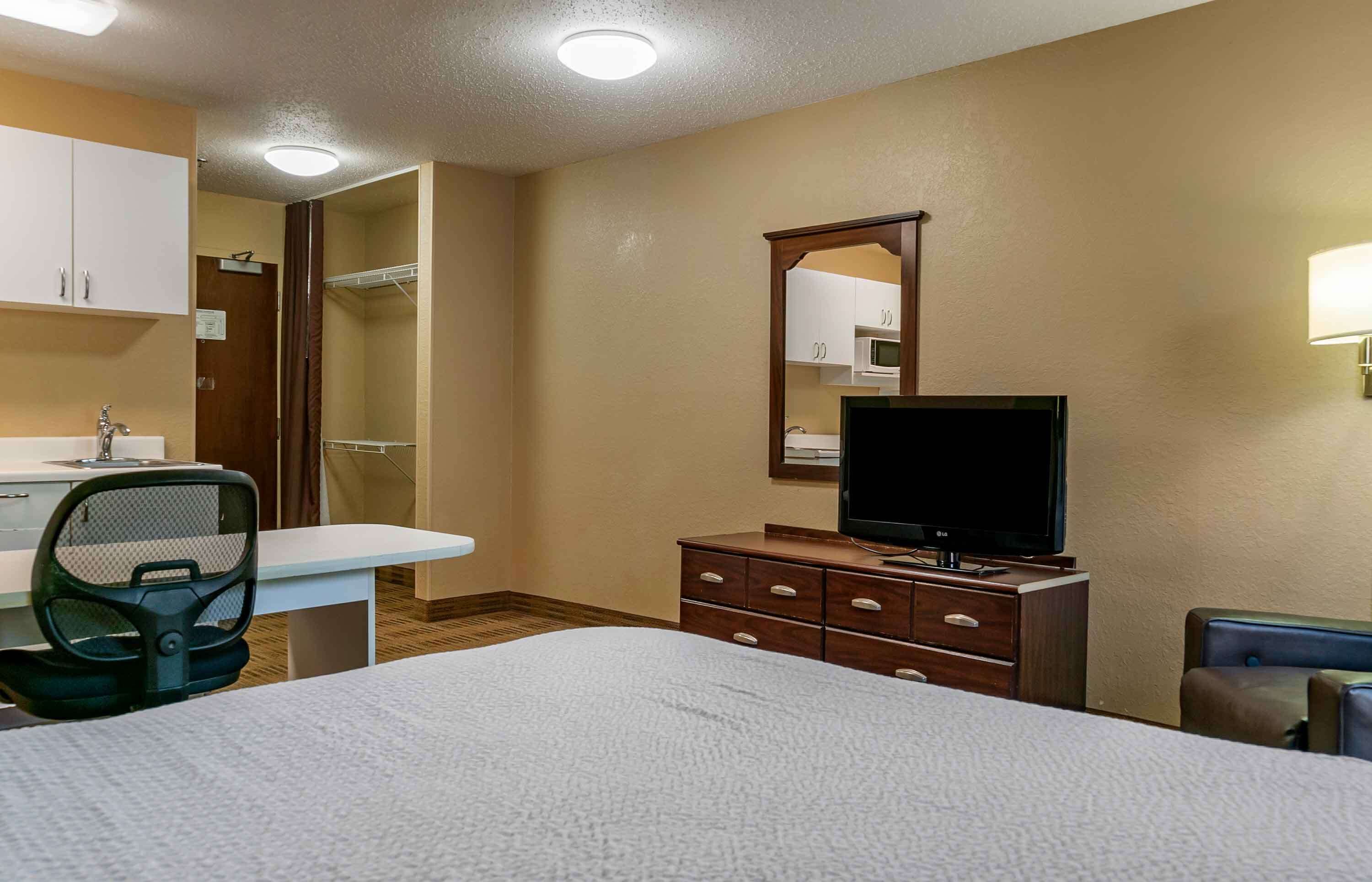 Ein Hotelzimmer mit Bett, Schreibtisch mit Stuhl, Fernseher, Kommode und Spiegel.