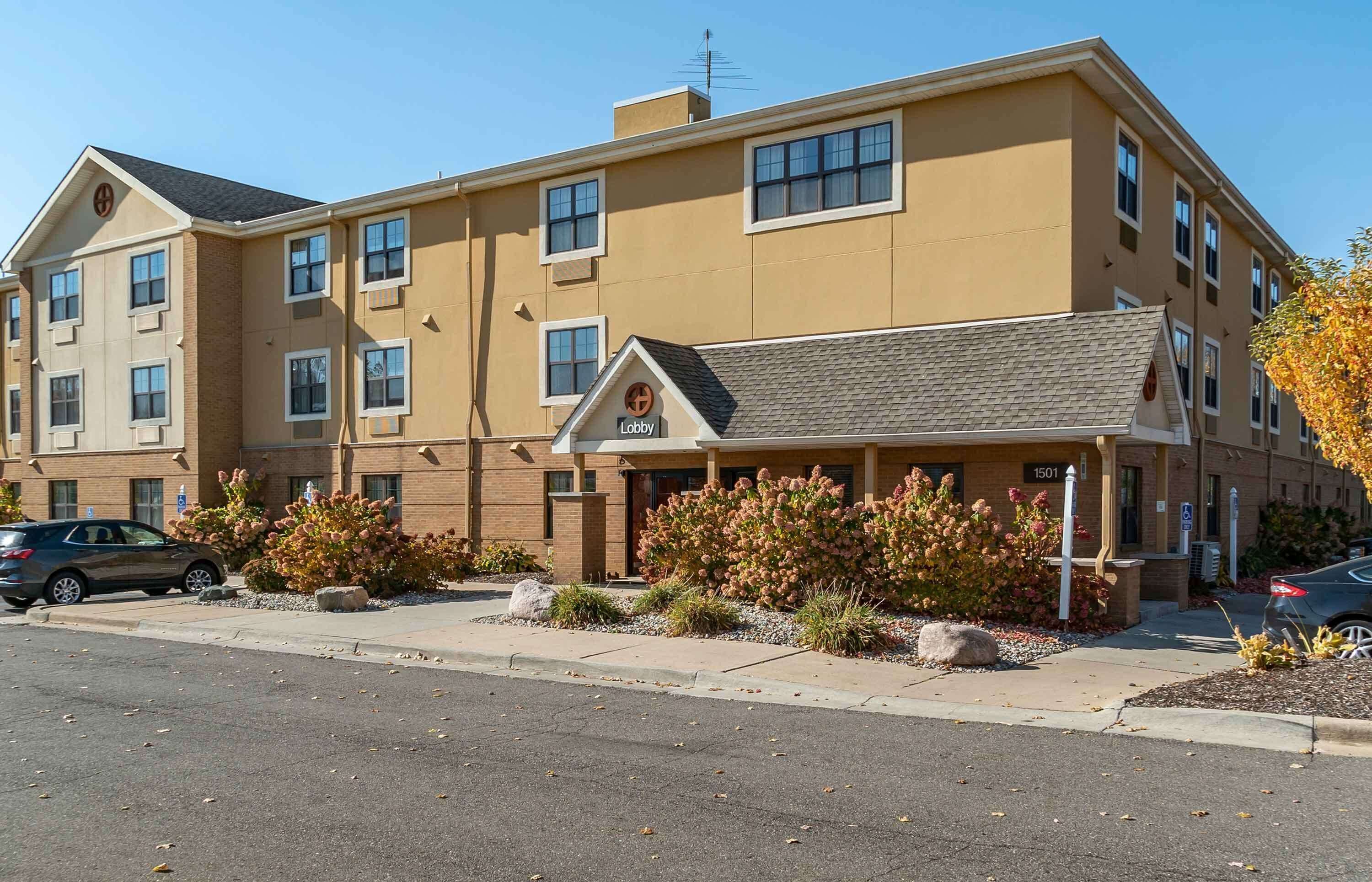 A multi-story hotel with a beige facade, a lobby entrance, and a parking lot with cars.
