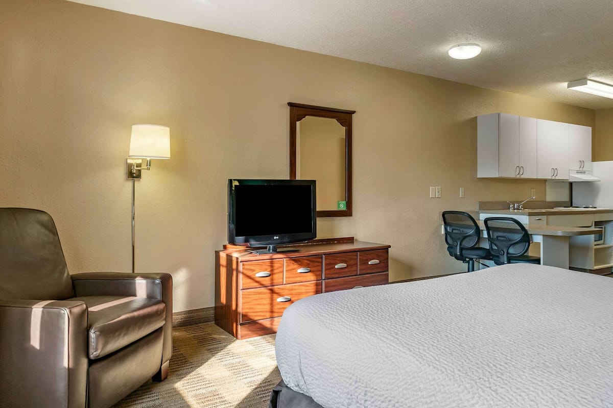 Ein Hotelzimmer mit Bett, Fernseher auf einer Holzkommode, Schreibtisch mit Stuhl und Spiegel an der Wand.