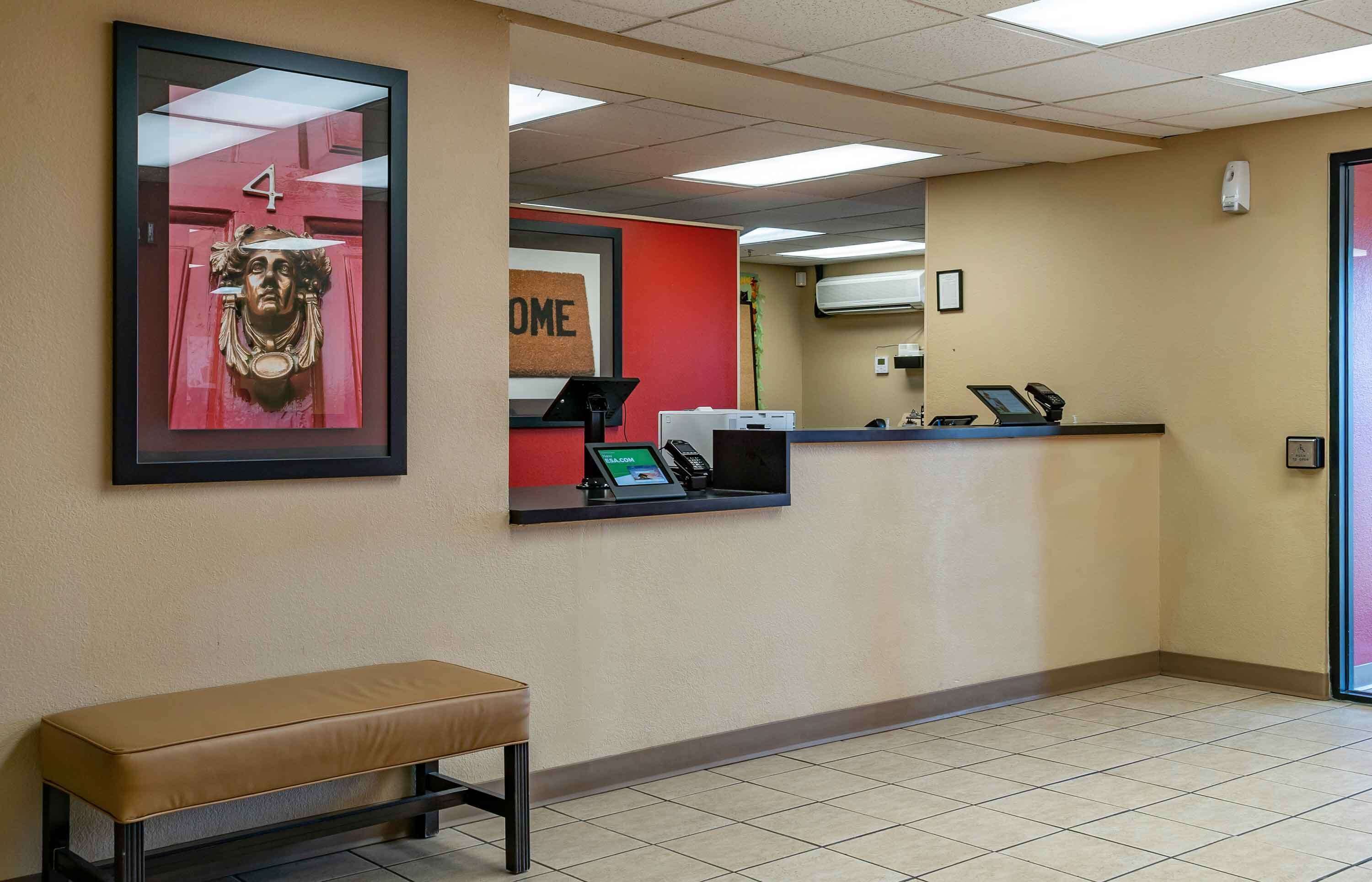 A reception area with a bench, a reception desk, a framed artwork, and a red door with a number.