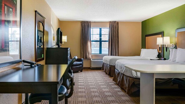 A hotel room with a bed, desk, chair, TV, and a window with curtains.