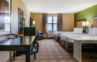 Una habitación de hotel con cama, escritorio, silla, televisor y ventana con cortinas.