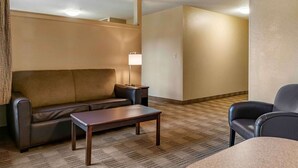 A hotel room with a sofa, a small table, a lamp, and a chair.
