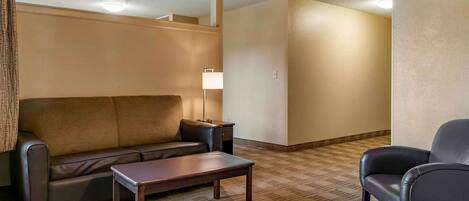 A hotel room with a sofa, a small table, a lamp, and a chair.