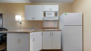 A compact kitchenette with white cabinets, a microwave, and a refrigerator. - Extended Stay America Suites Sacramento White Rock Rd (Rancho Cordova)