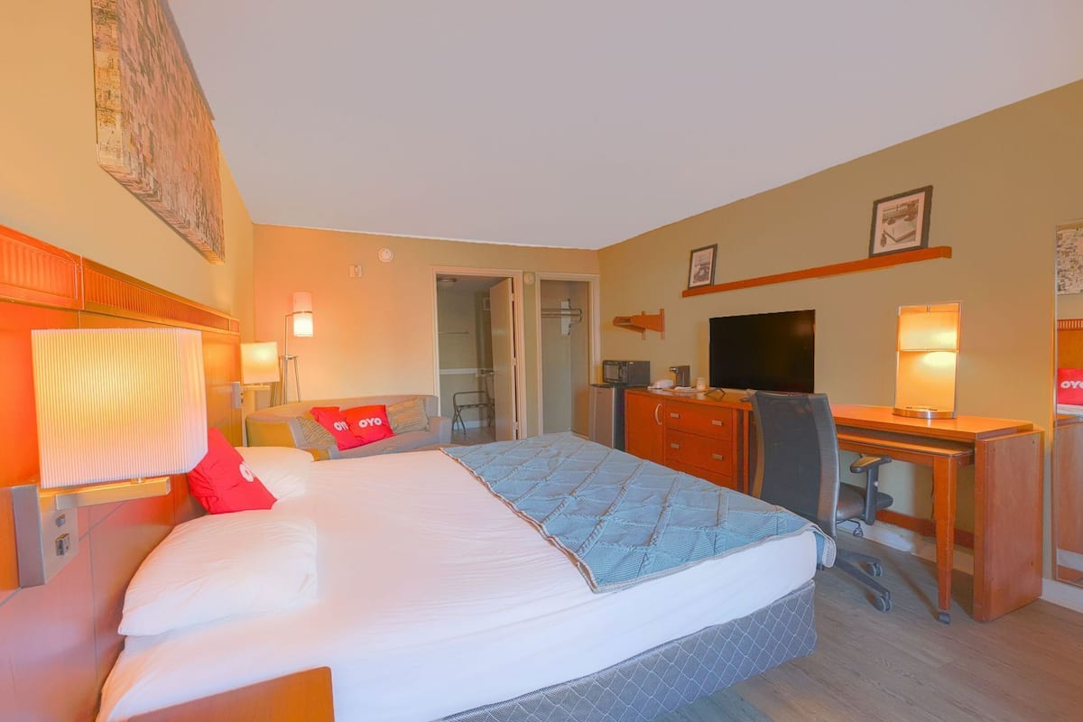 Habitación de hotel con cama, escritorio, televisión y baño visible a través de una puerta abierta.