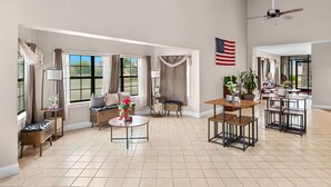 A spacious living room with a large window, a ceiling fan, and a dining area with multiple tables. - Americas Best Value Inn Brownsville West Tennessee (Brownsville)