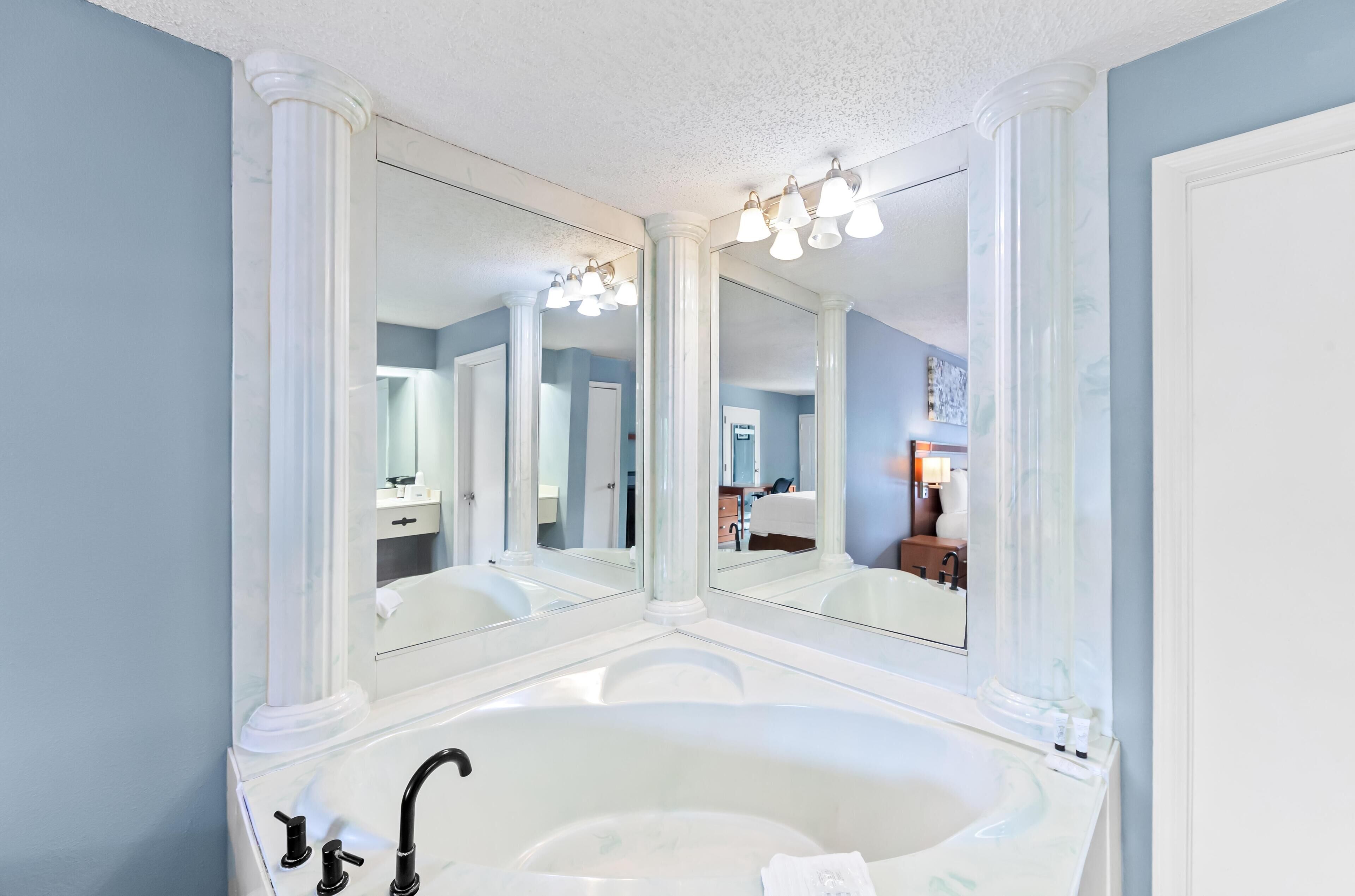 A bathroom with a large bathtub, a double sink, and a large mirror with lights.