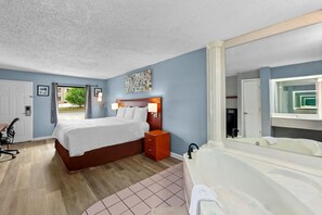 Un dormitorio con cama, mesita de noche, lámpara y un espejo grande que refleja un baño con bañera.