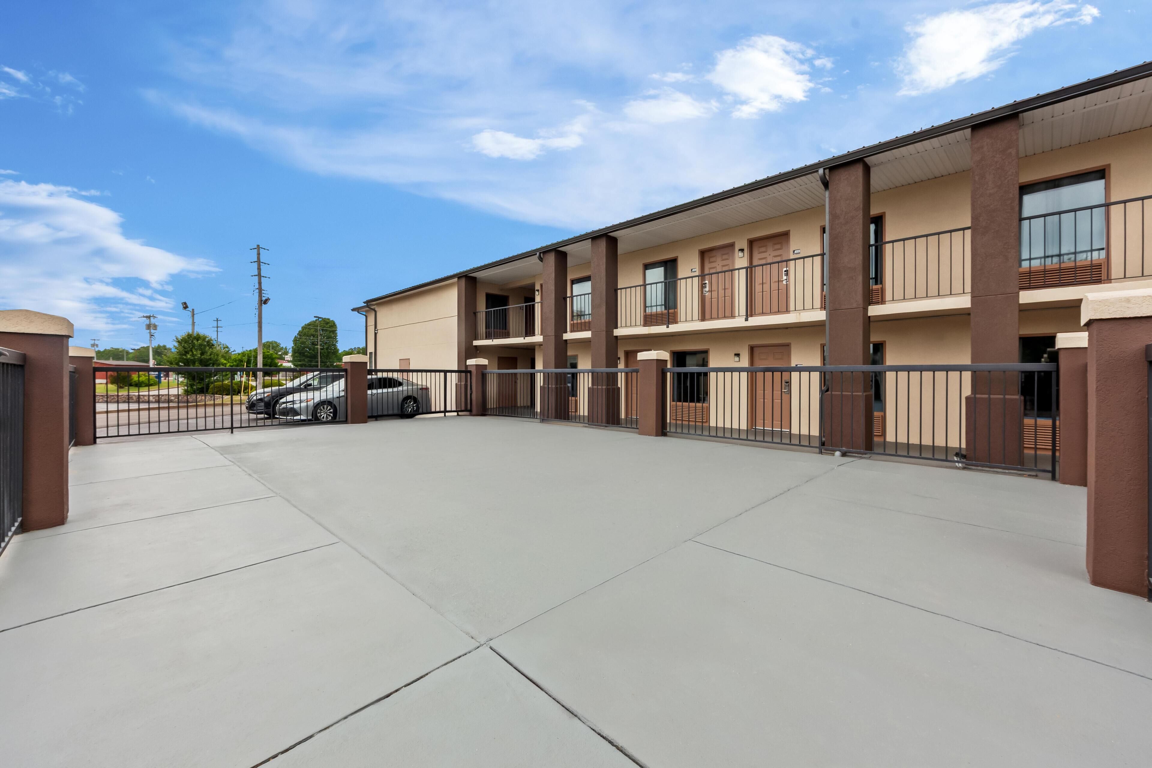 A multi-story building with a parking area, a gated entrance, and a clear sky.