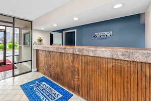Un’area reception con una scrivania in legno, un tappetino blu con il logo dell’hotel e una porta in vetro che dà sull’esterno.