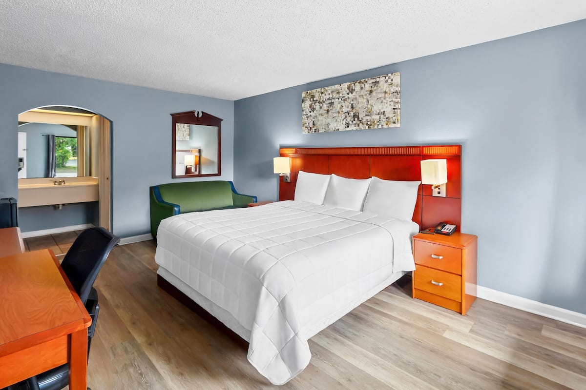 Una habitación de hotel con cama, mesita de noche, silla, escritorio y espejo.