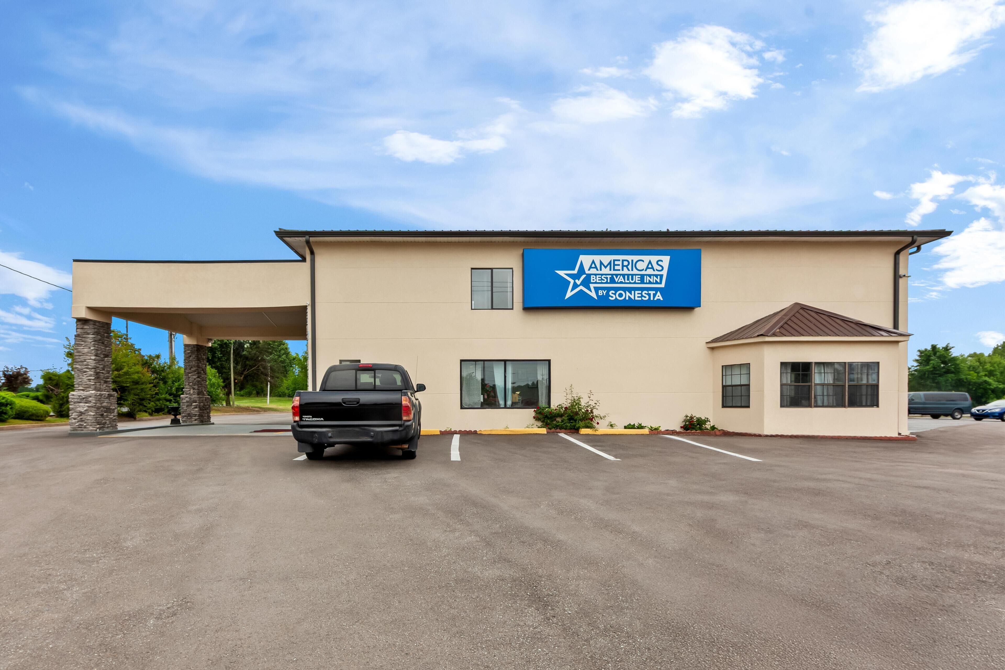 Un bâtiment sur lequel on peut lire l’inscription « AMERICAS BEST VALUE INN BY SONESTA », un parking et un camionnette noire.