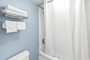 Un baño con una bañera blanca, una cortina de ducha y toallas en un perchero.