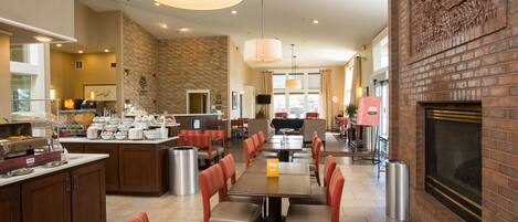 A hotel dining area with multiple tables and booths, a kitchen area, and a fireplace.