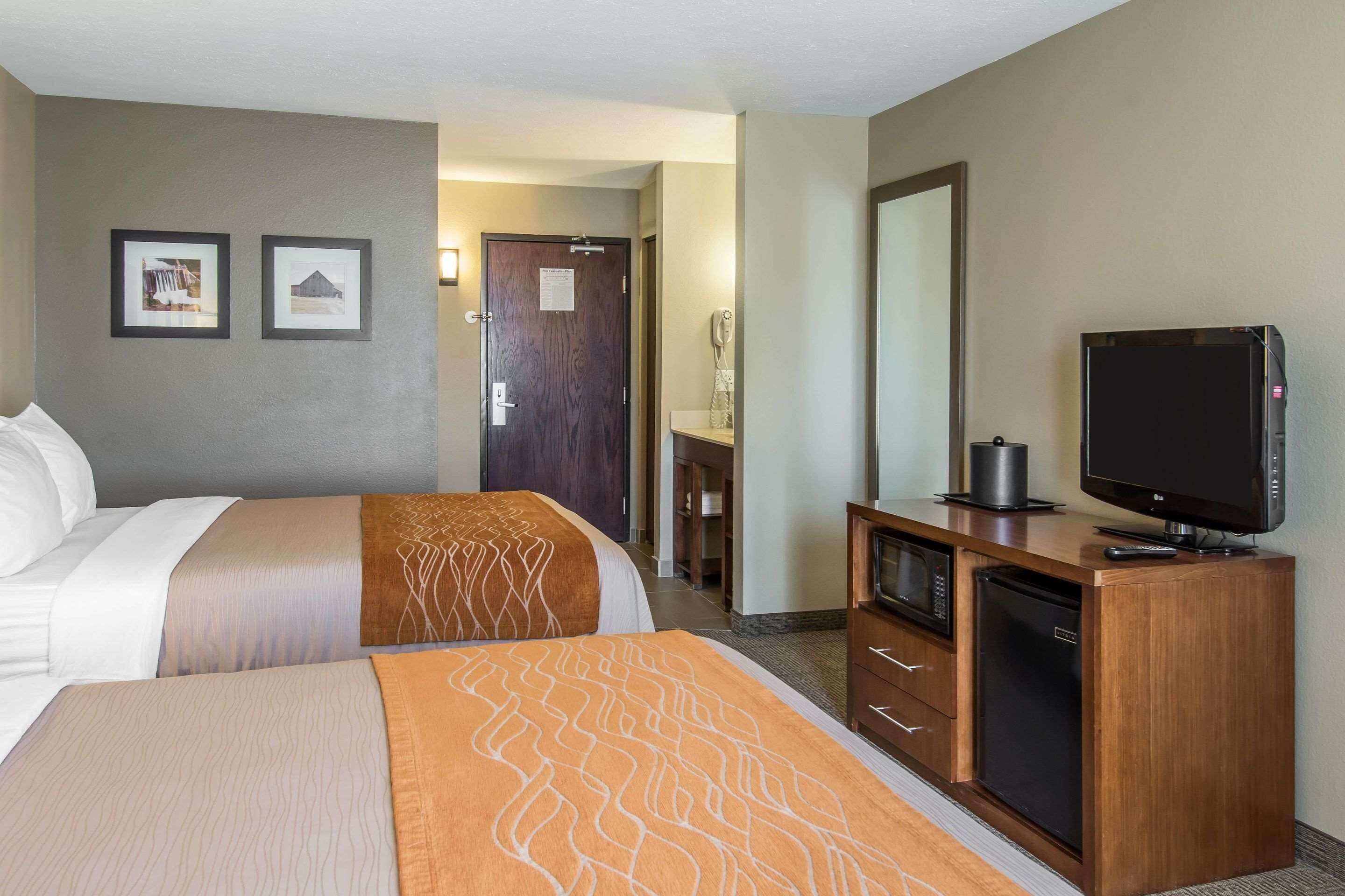 Une chambre d’hôtel avec deux lits, une télévision, un mini-réfrigérateur et une commode en bois.