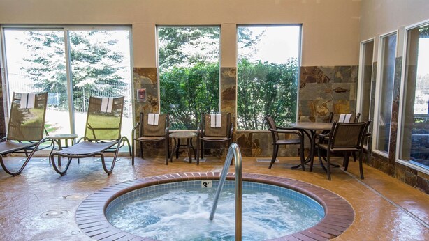 A hot tub surrounded by chairs and tables, with a stone wall and large windows offering a view of greenery. - Comfort Inn & Suites Spokane Valley Central (Spokane Valley)