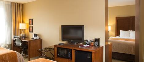 A hotel room with two beds, a desk with a computer, a television, a microwave, and a refrigerator.