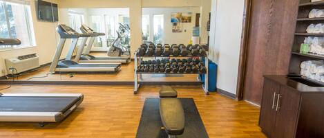Een sportschool met loopbanden, een bankdrukrek en gewichten.