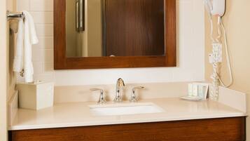 A bathroom with a wooden vanity, a large mirror, a sink, and a hairdryer mounted on the wall.