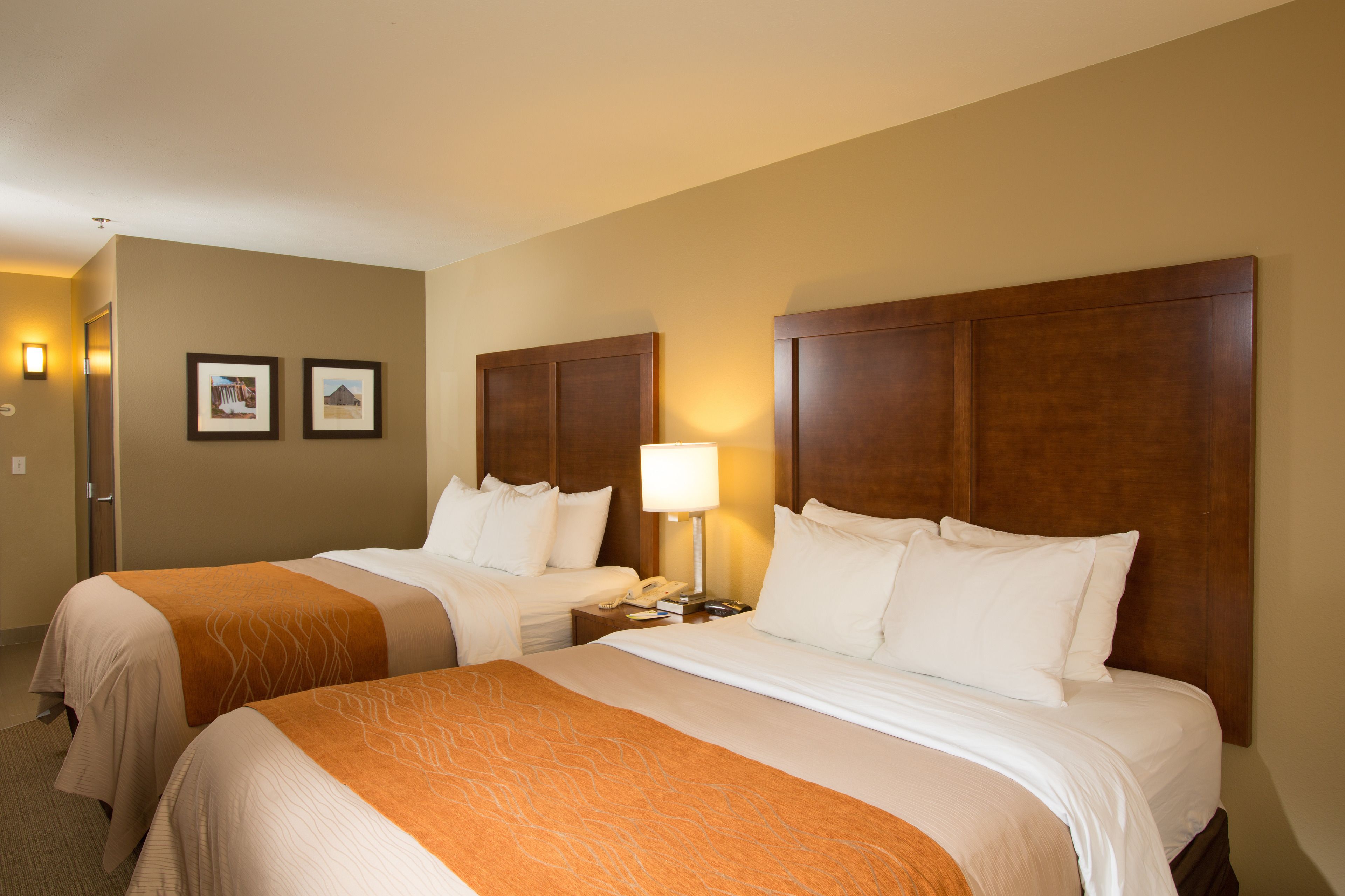 A hotel room with two beds, a nightstand, a lamp, and two framed pictures on the wall.